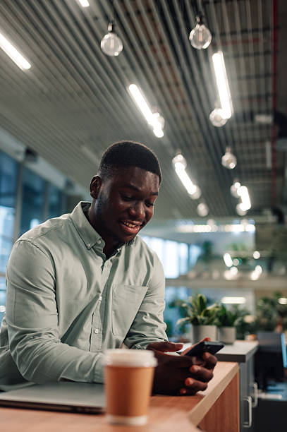 istock Young black man smiling using smartphone with coffee in office 2246253663