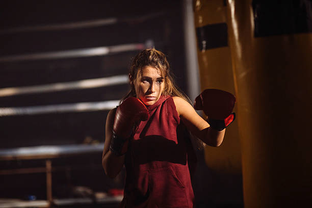 istock Focused Female Boxer In Red Outfit Throws Punch In Dim Gym Training Session 2246255137