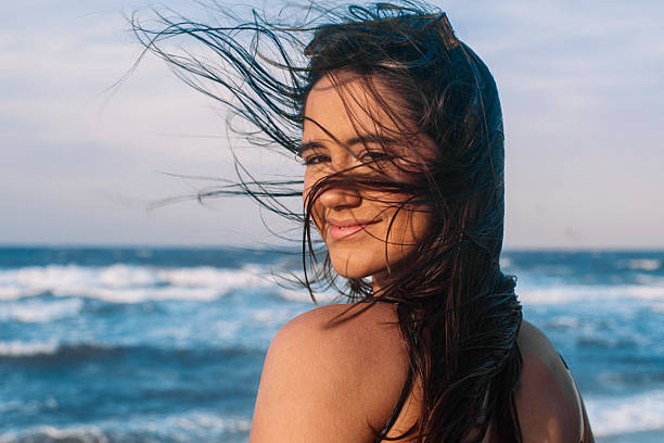 istock Smiling young woman by the ocean on a windy day 2246256182