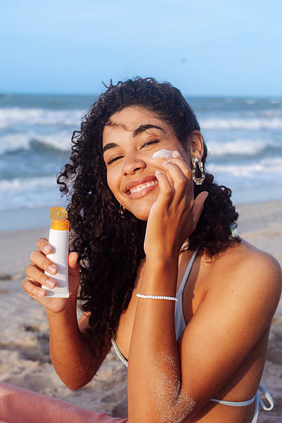 Young woman applying sunscreen on her face at the beach