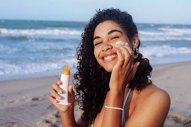 istock Young woman applying sunscreen on her face at the beach 2246256282