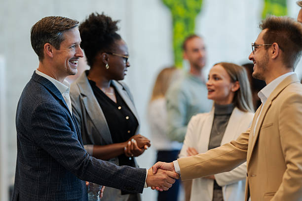 istock Businessmen shaking hands at corporate conference networking event 2246260440