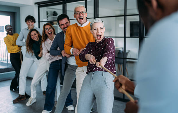 istock Playful colleagues having fun while playing tug-of-war in the office. 2246260762