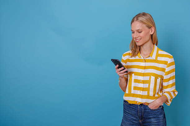 istock Woman smiling while using phone, checking social media, sending message or browsing internet on blue background 2246263176