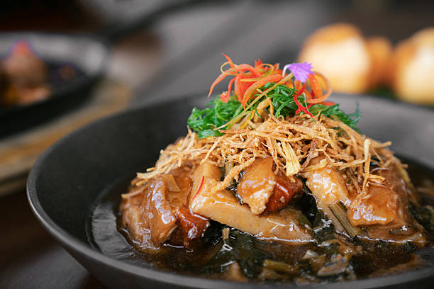 Close-up of braised pork belly served with Chinese kale and topped with crispy fried shallots and colorful garnish. The rich sauce and tender texture highlight the flavor of Asian cuisine, perfect for restaurant menus, food advertising, and editorial use.