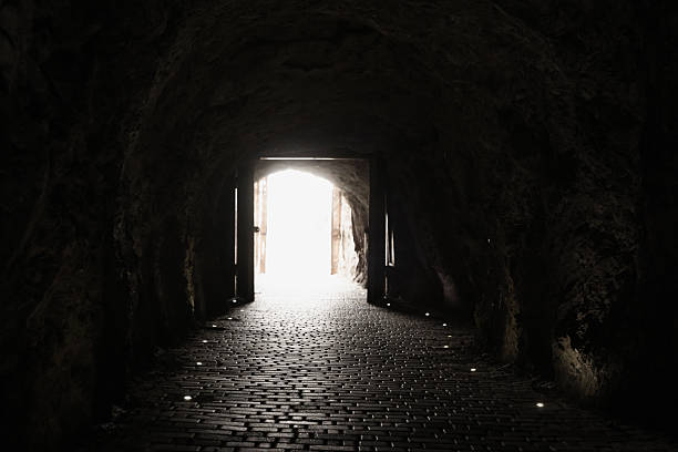 istock A dim underground tunnel with rough stone walls and a glowing exit at the end 2246297605