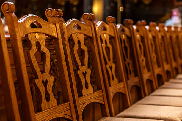 Close view of carved chair backs aligned in a long row. Soft warm lighting and deep bokeh highlight wood grain, ornament and a serene mood.
