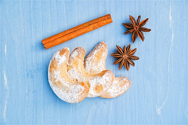 Cozy Christmas flat lay of powdered vanilla crescent cookies with cinnamon sticks and star anise on a rustic blue wooden surface. Copy space for text, directly above - Christmas, food and drink