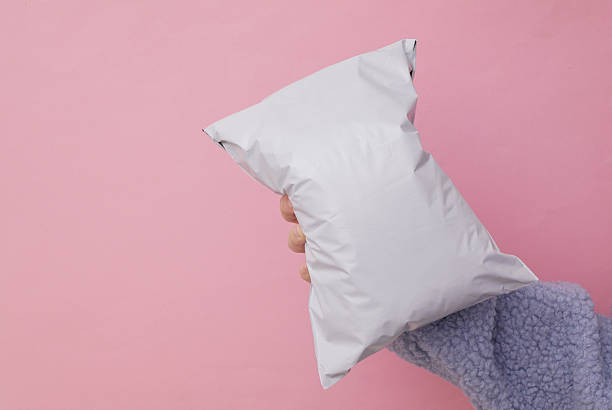 istock Female hand holding Empty blank white plastic parcel bag. Shipping Plastic Postal Packing Mockup on pink background 2246299437
