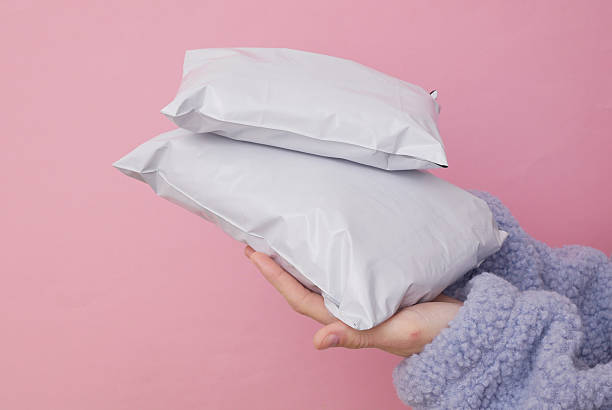 istock Female hand holding Empty blank white plastic parcel bags. Shipping Plastic Postal Packings Mockup on pink background 2246299441