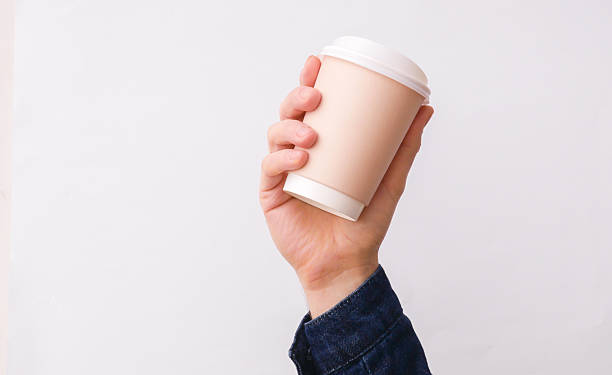 Hand holding disposable cardboard coffee cup on white background