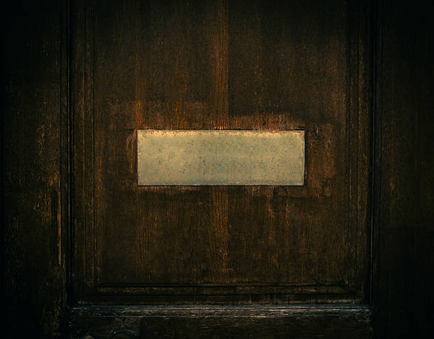 An old dark wooden door with a rectangular metal plate in the center for the occupant's name or room number, but it is currently empty and weathered.