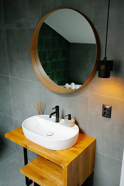 Modern bathroom interior with a round mirror, wooden vanity, and stylish sink, featuring a black faucet and ambient lighting.
