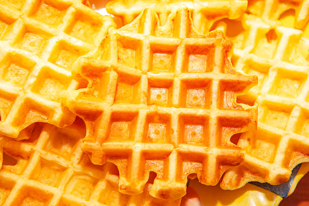 Golden waffles are stacked closely, showcasing their crisp texture and classic grid pattern. Warm lighting enhances their fresh, appetizing appearance, perfect for breakfast or food-themed visual