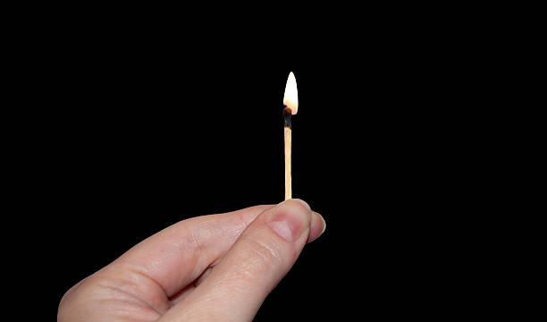 istock A burning match in hand. A match isolated in the black background. 2246307263
