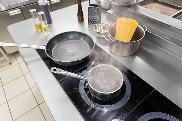 Pot of water boils on the stove as uncooked pasta waits nearby in a professional kitchen.