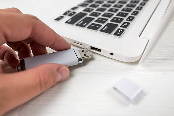 istock Hand inserting a USB flash drive into a laptop on a white background. Close-up of woman's hand plug USB flash drive on laptop at home. Copying data from a flash drive to a laptop 2246310754