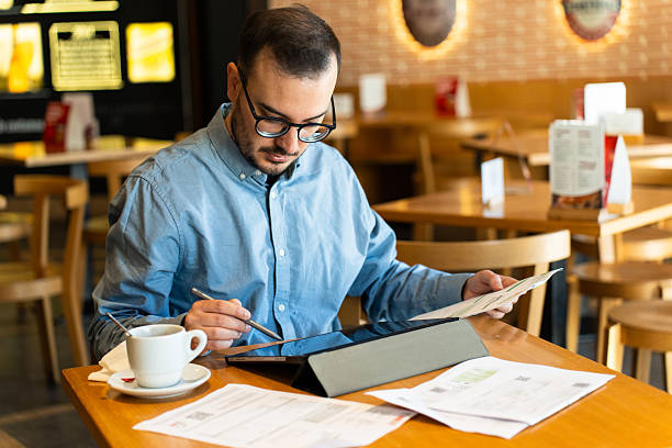 istock Man reviewing financial documents using tablet in coffee shop 2246317447