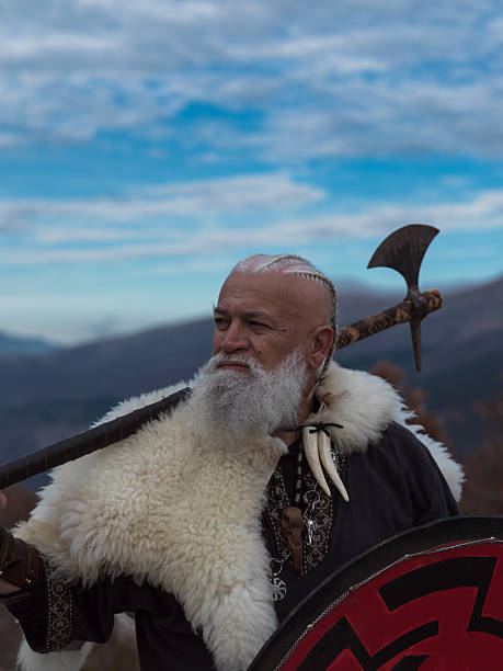 istock Bearded Viking warrior in fur cloak holding red shield and axe outdoors. Medieval Nordic fighter in traditional armor 2246320957