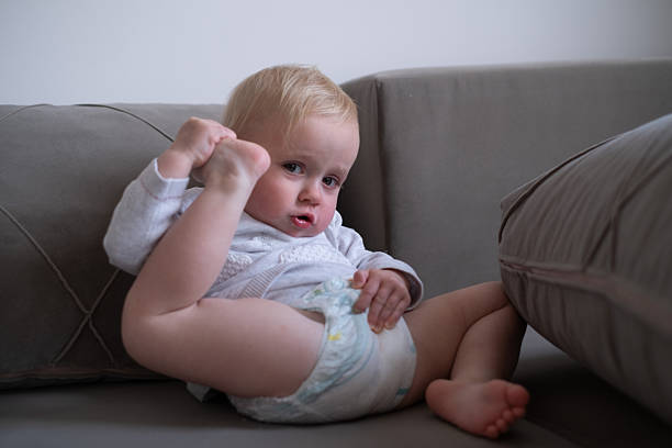 Shy happy child. Portrait of little cute toddler boy, baby in diaper calmly sitting and laughing isolated over white studio background. Concept of childhood, motherhood, life, birth. Copy space for ad