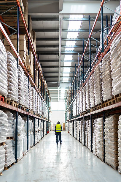 istock Warehouse worker walking down aisle with stacked goods 2246324433