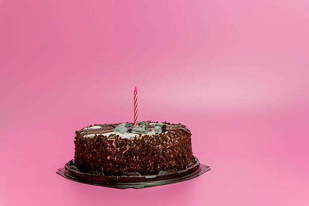 istock Chocolate cake with a single candle on top, placed on a black base, against a vibrant pink background, celebrating special occasions and joyful moments 2246329437
