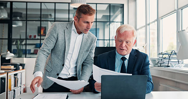 istock Document, business men and training with mentor for accounting, audit feedback or advice. Paperwork, mature manager or coaching with team in office meeting for financial bookkeeping, help or planning 2246329792