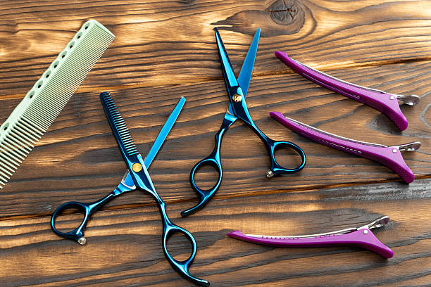 istock Professional hairdressing tools including blue scissors, pink clips, and a green comb arranged on a wooden surface, showcasing essential equipment for hairstyling and grooming 2246331268