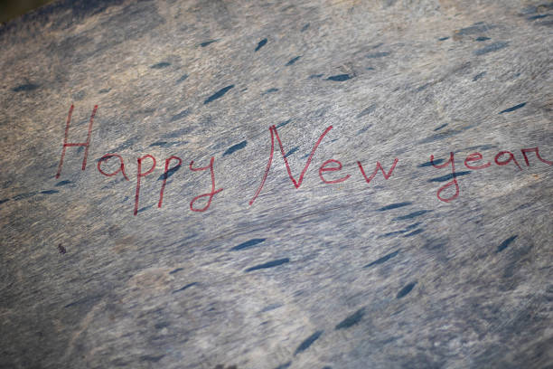 A close-up view of the words 'Happy New Year' written in red ink on a dark, textured surface, conveying a festive holiday wish.