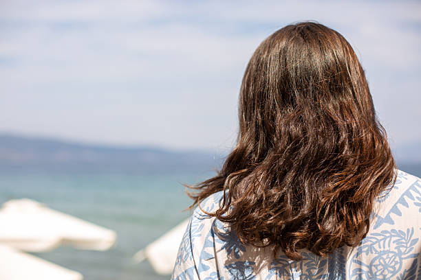 Woman with wavy brown hair looking out at the calm blue sea and distant horizon