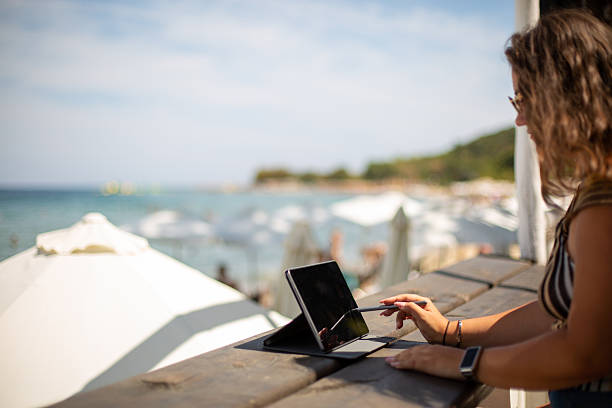 istock Young woman remote working with tablet at beach cafe 2246338931