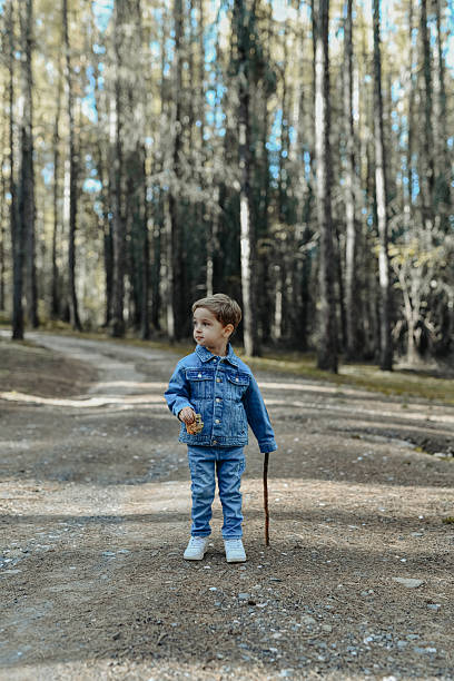 istock Young Boy in Denim Jacket Eating Cookie Outdoors in a Forest Setting 2246339709