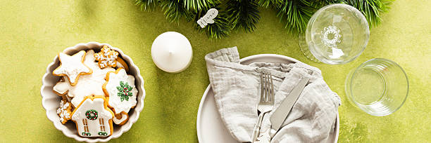 istock A festive Christmas table setting with an empty plate, cutlery, and napkin on a bright green background, decorated with spruse and white tree ornaments, banner 2246340673