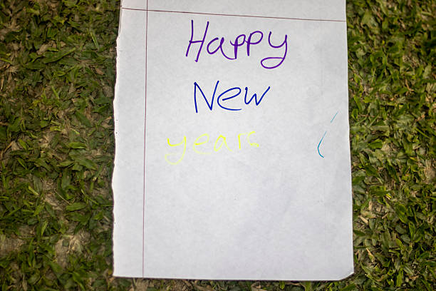 A handwritten 'Happy New Year' message on a piece of lined paper, placed on a patch of green grass, symbolizing a fresh start and hopeful wishes for the upcoming year.