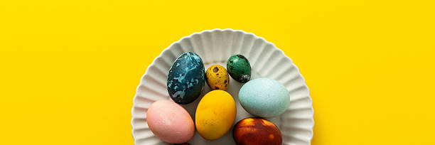 istock A variety of beautifully painted Easter eggs in different colors and patterns are placed on a delicate white plate. The vibrant hues stand out against the cheerful yellow backdrop, banner 2246341582