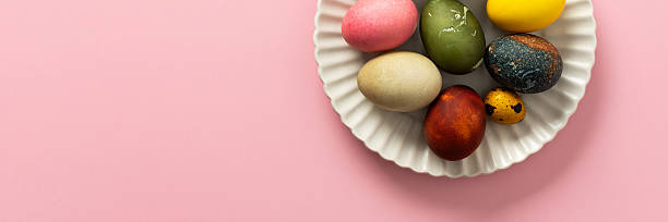 istock A variety of decorated Easter eggs are arranged on a circular plate against a soft pink background, showcasing vibrant colors and intricate designs for a seasonal celebration, banner 2246341591