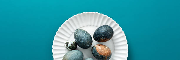 istock Decorative Easter eggs with various textures and colors are arranged neatly on a white plate, resting on a vibrant teal surface, creating a festive spring atmosphere, banner 2246341593