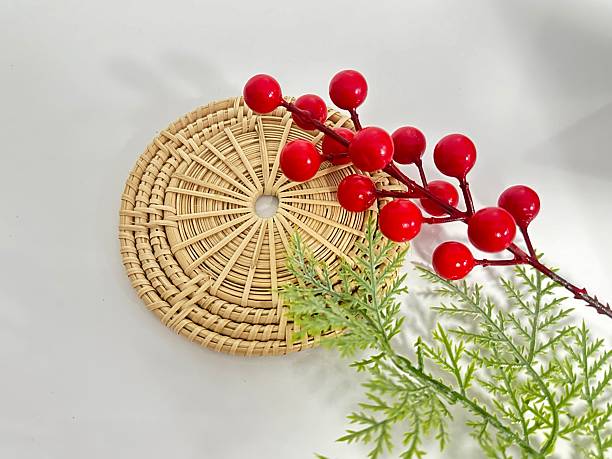 istock Decorative Rattan Coaster with Red Berries and Green Leaves Arranged on a White Surface for Stylish Home Decor and Seasonal Themes 2246342639