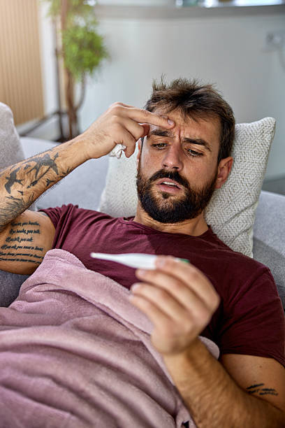 istock Sick man lying on sofa checking his temperature at home in the living room. 2246344025