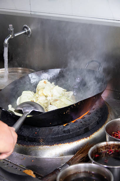 Stir fry cabbage in wok over gas stove with steam and ladle