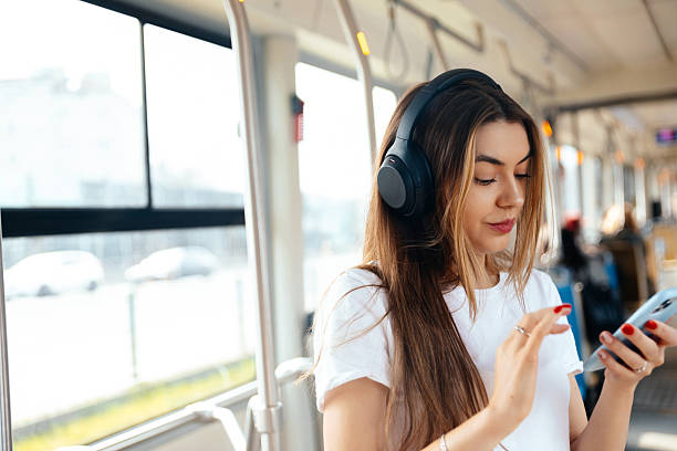 istock Young woman enjoying music on headphones while using smartphone in public transport setting with urban background lifestyle concept 2246347426