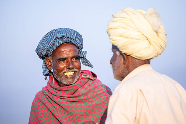 Pushkar, Rajasthan, India - November 2024: Portrait of a rajasthani male in traditional white clothes with colourful turban at desert fair ground along with camel during the pushkar camel fair to trade camels.