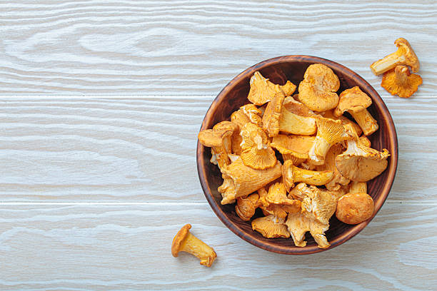 istock Fresh chanterelle mushrooms in a a rustic bowl on white wooden table top view, space for text 2246357246