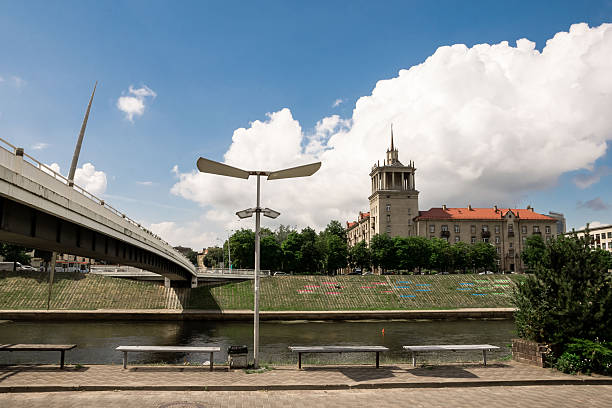 Vilnius, Lithuania - July 01, 2015 - Scenic urban riverfront with historic architecture and bridge under blue sky.