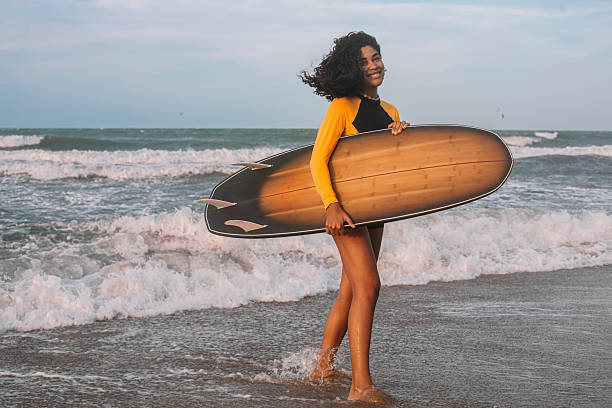 istock Young woman walking with a surfboard by the ocean 2246361493