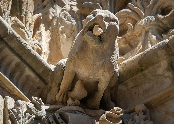 Low angle shot of a stone gargoyle and heraldic coat of arms on an ornate facade in Salamanca showing Gothic architectural detail under bright daylight.