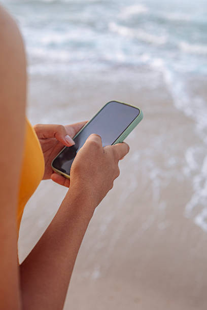 istock Close-up of hands holding smartphone by the beach 2246365426
