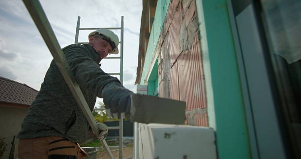 istock Cleaning insulation panel on exterior wall with trowel, construction worker in safety gear working on brick building, close-up of masonry work on ladder with helmet and gloves 2246367244
