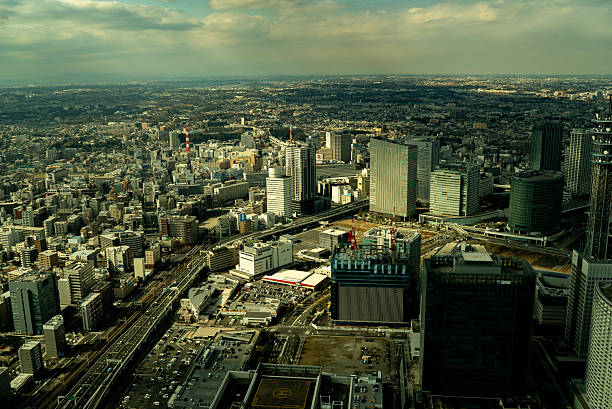 Yokohama, Japan Febuary 25, 2016. Panoramic aerial view of a sprawling urban area with high-rises, industrial zones, highways, and a dramatic cloudy sky, taken from an elevated vantage point.
