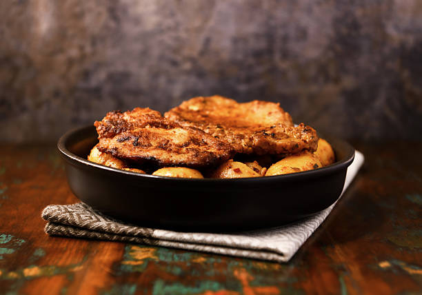 Fried pork steaks in a frying pan with potatoes. Rustic wooden background. Soft focus.